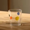 Collection de verres à eau originaux et carafes à pois colorés, disposés sur une table rustique pour un effet rétro chic.
