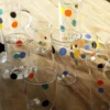 Gros plan sur un verre à eau original transparent orné de pois orange, jaune et bleu, idéal pour l’eau fraîche ou le jus.