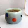Verre à eau coloré en céramique mate avec pois rouge, offrant une texture douce au toucher et un look chaleureux.