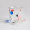 Verre à eau coloré avec pois multicolores rouges, bleus et jaunes, posé sur une coupelle assortie en verre transparent.
