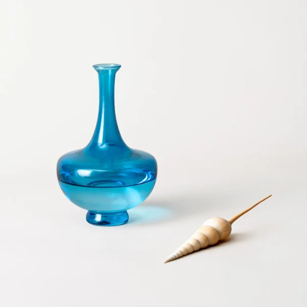 Élégante bouilloire en verre bleu placée在livre de style, à côté d’un verre et d’un coquillage sculpté.
