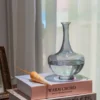 Bouilloire en verre transparente posée sur un livre de décoration, avec un coquillage en bois à côté.