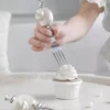 Gros plan sur la cuillère et la fourchette de couverts à dessert ornés de coquillages nacrés, accompagnés de perles décoratives.