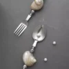 Ensemble de couverts à dessert décorés avec des coquillages naturels sur manche en métal, posés sur une surface noire élégante.