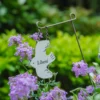 Décoration de pot de fleur en forme d’oiseau blanc suspendu parmi des fleurs violettes dans un jardin champêtre.