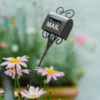 Boîte aux lettres en métal foncé dans un pot fleuri, parfaite comme décoration pot de fleurs nostalgique.