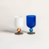 Deux verres à vin artisanaux soufflés à la bouche, posés sur une table blanche avec tranche de citron et décoration estivale.
