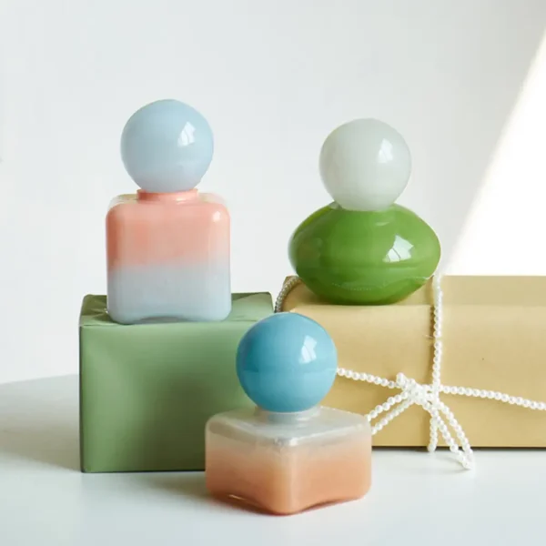 Trois diffuseurs de parfum en verre aux teintes douces posés sur des boîtes cadeaux pastel.