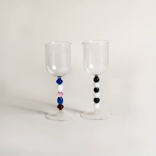 Deux verres à eau design contrastés par leur pied, présentés avec une bouteille de vin aromatisé.