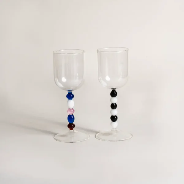 Deux verres à eau design contrastés par leur pied, présentés avec une bouteille de vin aromatisé.
