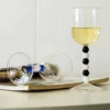 Gros plan sur la tige perlée d’un verre à eau design, avec reflets lumineux sur fond de magazine lifestyle.