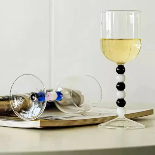 Gros plan sur la tige perlée d’un verre à eau design, avec reflets lumineux sur fond de magazine lifestyle.