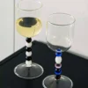 Verre à eau design aux perles multicolores, posé sur une table noire à côté d’un second verre assorti.