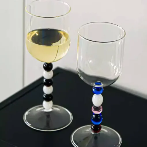Verre à eau design aux perles multicolores, posé sur une table noire à côté d’un second verre assorti.