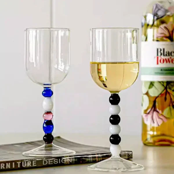 Duo de verres à eau design aux perles noires et blanches, rempli de vin blanc dans un intérieur moderne.