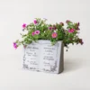 Pot de fleur en forme de livre blanc avec fleurs violettes, parfait pour la décoration intérieure ou extérieure.