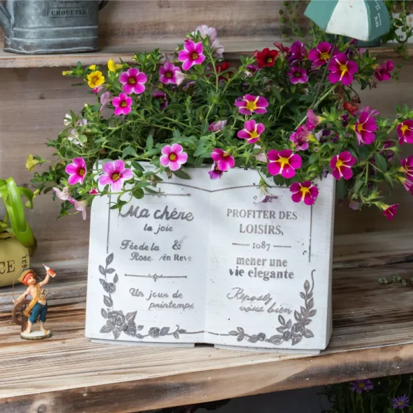 Pot de fleur décoratif en résine blanche, posé sur une étagère en bois avec des fleurs épanouies.