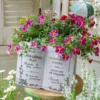 Pot de fleur en résine blanche avec design livre, entouré de marguerites dans un décor champêtre.