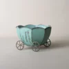 Pot de fleur intérieur vert en forme de carrosse, orné de fleurs violettes dans un décor naturel en plein air.