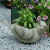 Pot de fleur intérieur en forme d'oiseau, utilisé pour planter des fleurs fraîches dans un décor extérieur fleuri.