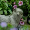 Gros plan sur un pot de fleur intérieur en forme d’oiseau, entouré de fleurs roses et feuillages.