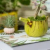 Détail du bec du pot de fleur jaune en forme de bananier, avec ornements miniatures.