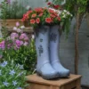 Bottes décoratives servant de pot de fleur pour extérieur, posées sur un tabouret en bois dans un coin fleuri de jardin.