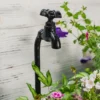 Robinet en fonte noire sur pot de fleur pour balcon, entouré de feuillage et de fleurs printanières.