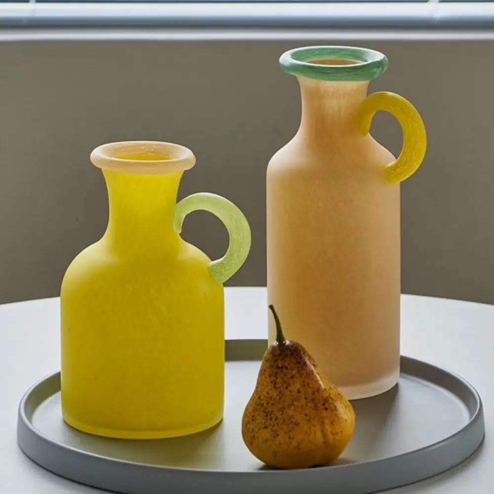 Vases en verre sculptural avec poignée incurvée, inspirés des amphores revisitées dans une esthétique contemporaine.