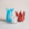 Trois vases en verre soufflé – blanc, bleu et corail – présentés ensemble sur une table lumineuse pour une mise en scène artistique autour des vases et fleurs.