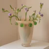 Grand vase artisanal beige décoré de perles vertes, parfait pour sublimer une composition florale sur une console moderne.