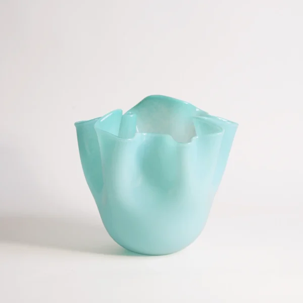 Vase art déco turquoise en verre soufflé, mis en valeur avec des fleurs blanches et une lumière naturelle douce sur fond de stores.