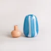 Vase rayé bleu allongé couché sur le côté, montrant ses lignes blanches douces et harmonieuses.